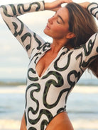 Woman wearing a zipped up swimsuit with green geometric patterns against a beach background