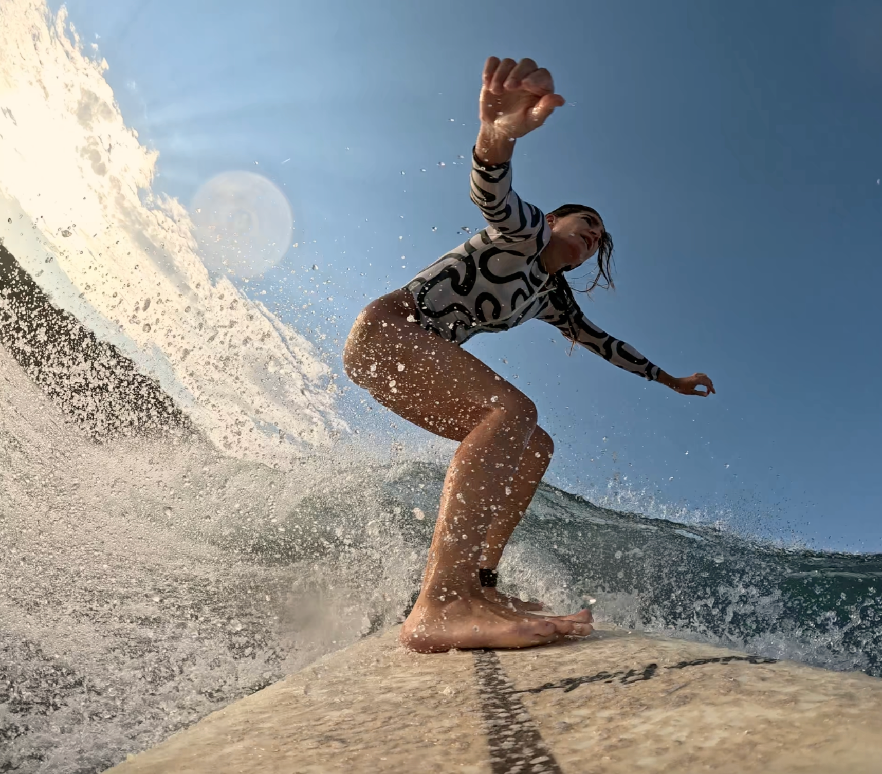 Woman surfing on a wave wearing a swimsuit with a clear blue sky